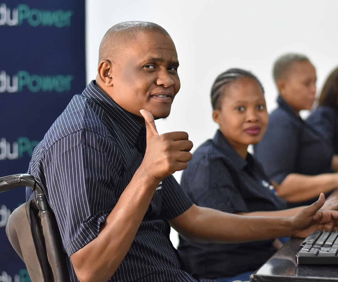 EduPower learner in a wheelchair giving a thumbs-up alongside classmates in a contact centre training room